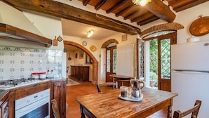 A rustic kitchen with a gas stove, wooden cabinets, and a dining table with chairs.