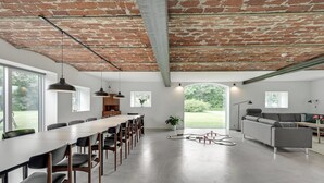 A spacious, modern interior with a long dining table, a sofa, and a large window offering a view of the outdoors. - 7 bedroom stunning apartment in Varde (Varde)