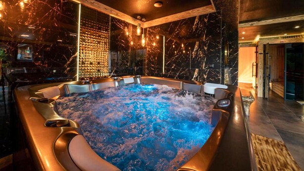 Un jacuzzi con interior de mármol, rodeado de detalles de madera e iluminación ambiental.