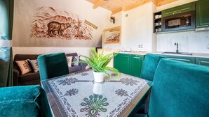 Un comedor con una mesa dispuesta para dos personas, un sofá verde y un mural en la pared.