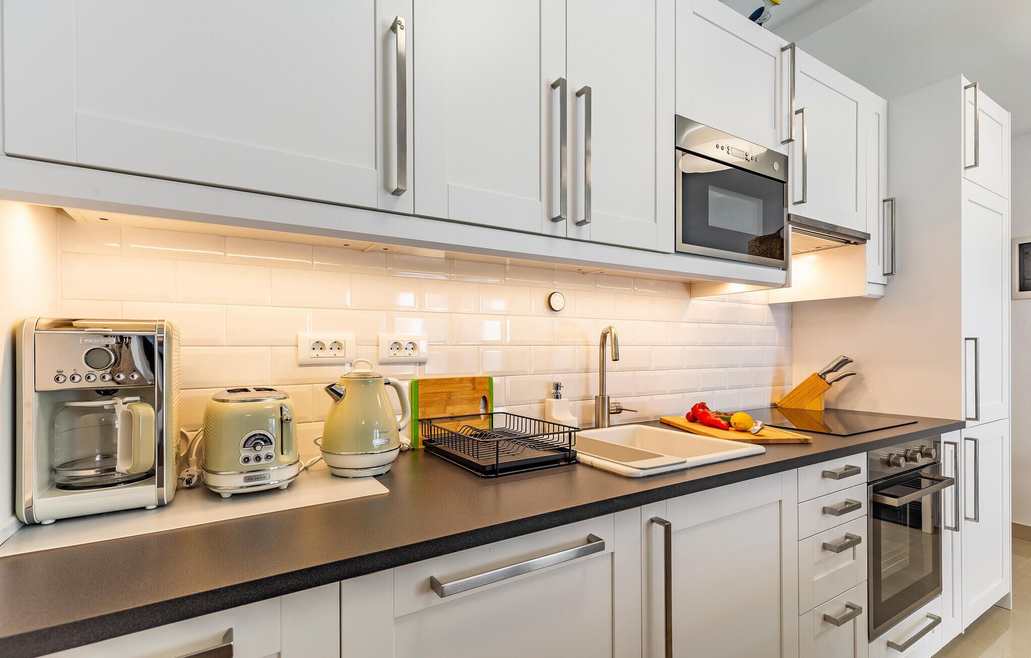 Una cocina moderna con armarios blancos, electrodomésticos de acero inoxidable y encimera negra.
