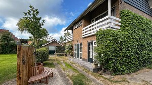 A two-story brick house with a balcony, a wooden bench, and a well-maintained garden. - 1 bedroom nice apartment in Zoutelande (Zoutelande)