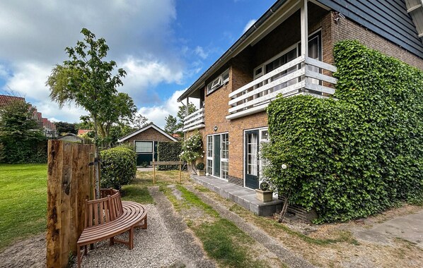 Een tweelaags bakstenen huis met een balkon, een houten bankje en een verzorgde tuin.