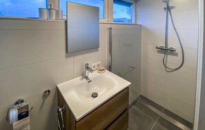 Een moderne badkamer met een wit wastafelmeubel, een spiegel erboven en een douche met een handdouche.