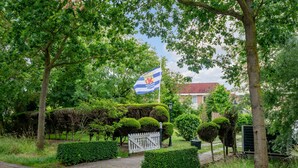A pathway leading to a gated entrance with a flag, surrounded by lush greenery and trees. - 1 bedroom nice apartment in Zoutelande (Zoutelande)