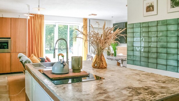 Una cocina moderna con una isla grande, horno empotrado y salpicadero de azulejos verdes.