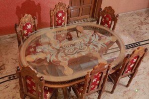 Ein runder Tisch mit Glasplatte, umgeben von kunstvoll geschnitzten Holzstühlen, jeweils mit roter und weißer Blumenstoffpolsterung.
