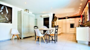 A modern kitchen with white cabinetry, a dining table with chairs, and a large painting on the wall. - Amazing home in St Victor la Coste (St Victor la Coste)