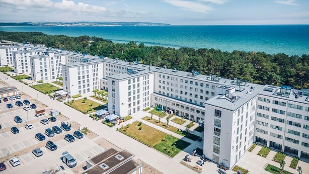 Un moderno complejo de apartamentos con varios edificios, un estacionamiento y vista al mar.