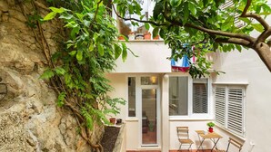 Una habitación pequeña con paredes blancas, una puerta de vidrio corredera, una ventana con contraventanas y una mesa pequeña con dos sillas.