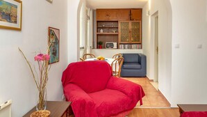 Un salón acogedor con un sofá rojo, una mesa de comedor con sillas, una zona de cocina con armarios y un microondas, y un pasillo que lleva a otra habitación.