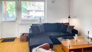 Un salon moderne avec un canapé bleu foncé, une table basse en verre et une vue sur un immeuble à travers de grandes fenêtres.