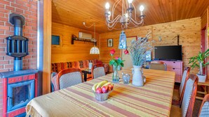 Ein gemütliches Holzhaus-Interieur mit Esstisch, Stühlen, einer Pendelleuchte, einem Kamin und einem Fernseher.