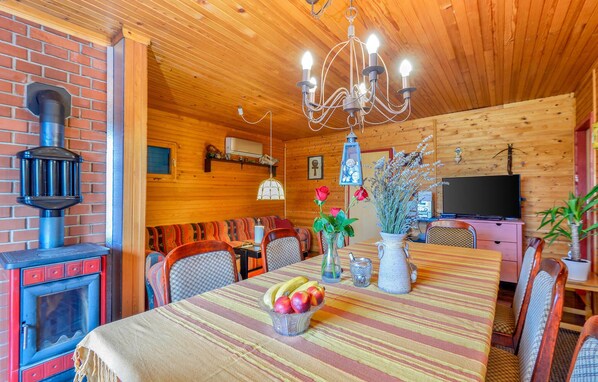 A cozy wooden cabin interior with a dining table set, chairs, a chandelier, a fireplace, and a television. - Stunning home in Kneginec with sauna (Kneginec)
