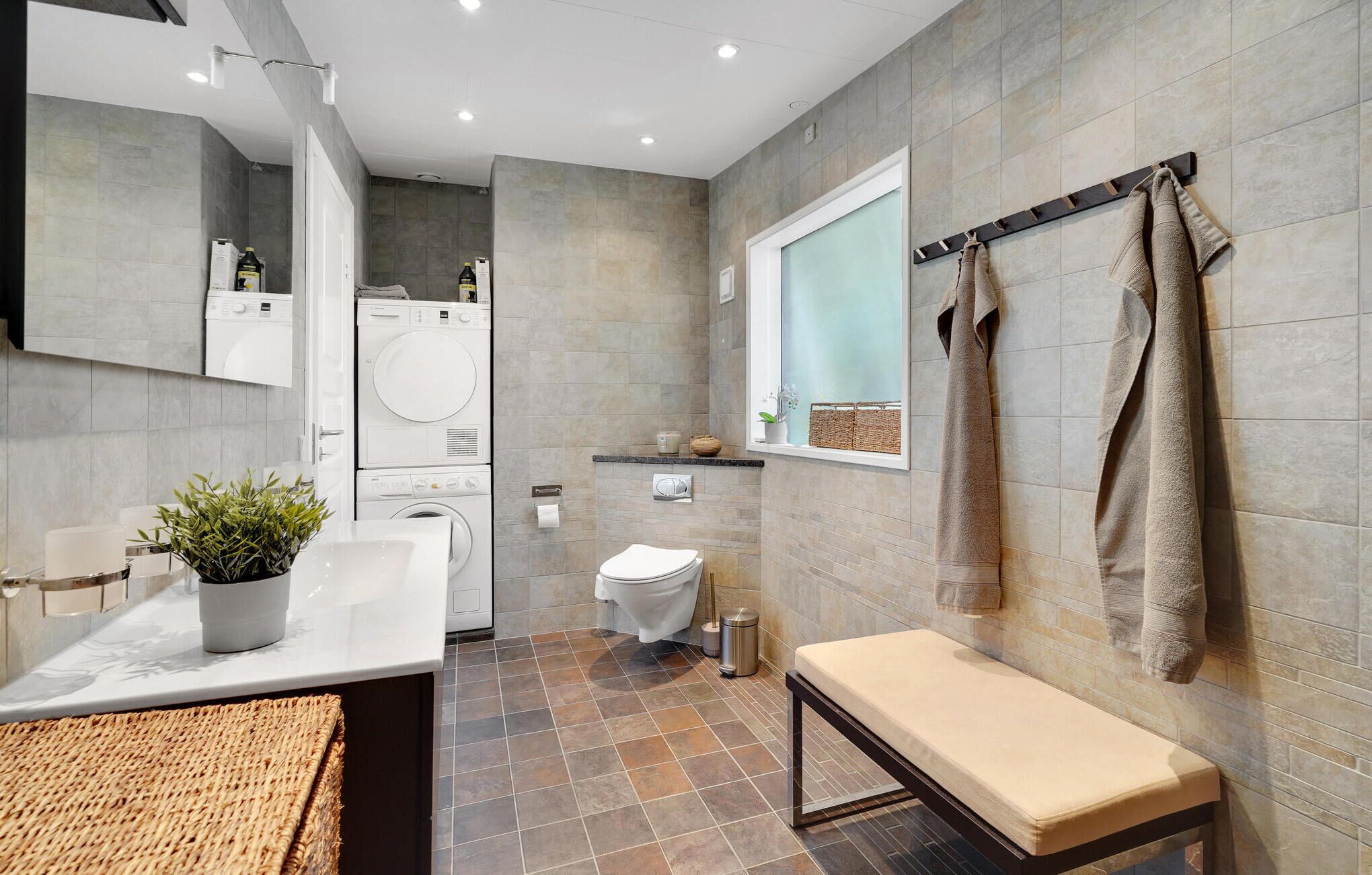 A modern bathroom with a sink, mirror, toilet, and bench.