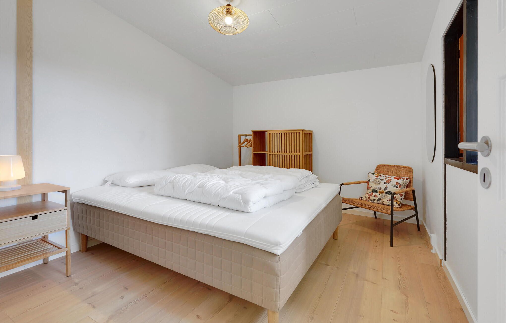 Un dormitorio con una cama, una mesita de noche de madera, una silla y una lámpara colgante.