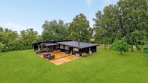 A modern house with a wooden deck, outdoor seating, and a covered patio. - 4 bedroom amazing home in Væggerløse (Væggerløse)