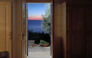 An open door leading to a balcony with a view of the sea and a potted plant.