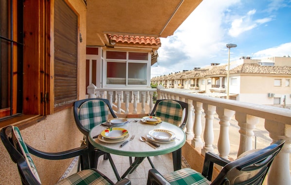 A balcony with a table set for two, chairs, and a window overlooking a row of buildings. - 2 bedroom cozy apartment in San Pedro del Pinatar (San Pedro del Pinatar)