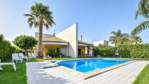 A swimming pool with a tiled deck, surrounded by palm trees and a well-maintained lawn. - Beautiful apartment in S. Croce Camerina RG (S. Croce Camerina RG)