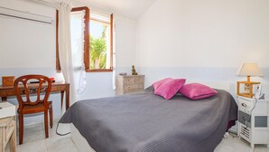 Un dormitorio con cama, escritorio, silla, mesita de noche y ventana con cortinas.