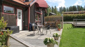A wooden deck with outdoor seating, a red awning, and a view of a forested area.