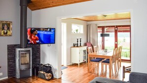 A living room with a fireplace, a television, a dining area, and a view of the outdoors.