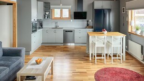 A modern kitchen with grey cabinets, a built-in oven, and a dishwasher. There is a dining area with a wooden table and white chairs.
