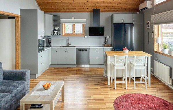 A modern kitchen with grey cabinets, a built-in oven, and a dishwasher. There is a dining area with a wooden table and white chairs.