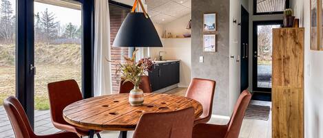 A dining area with a round wooden table, six chairs, a black lamp, and a view of the outdoors.