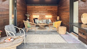 Een knus houten vakantiehuisje met een zithoek, voorzien van rieten meubels en een stenen vloer.
