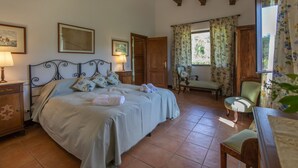 Un dormitorio con una cama grande, una mesita de noche de madera, una silla y una ventana con cortinas.