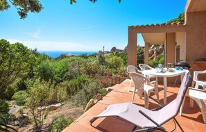Une terrasse avec une table et des chaises donnant sur un vignoble et la mer.