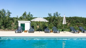 Una piscina con lettini e ombrelloni, circondata dal verde.