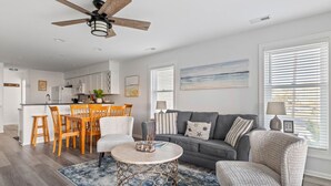 A modern living room with a grey sofa, a round coffee table, and a dining area with wooden chairs. - Oceanview Townhouse w/ Pool - Newly Renovated (Surf City)
