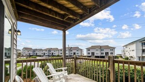 A wooden deck with two Adirondack chairs, a lifebuoy, and a view of residential buildings in the background. - Oceanview Townhouse w/ Pool - Newly Renovated (Surf City)