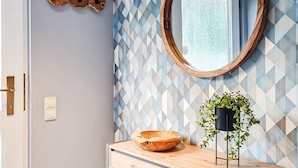 A bathroom with a geometric patterned wall, a wooden bowl on a vanity, a potted plant, and a round mirror. - Ferienhaus 16 in Kirchheim (Kirchheim)