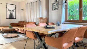A modern living room with a wooden dining table, cushioned chairs, a sofa, and a cactus plant. - Ferienhaus 16 in Kirchheim (Kirchheim)