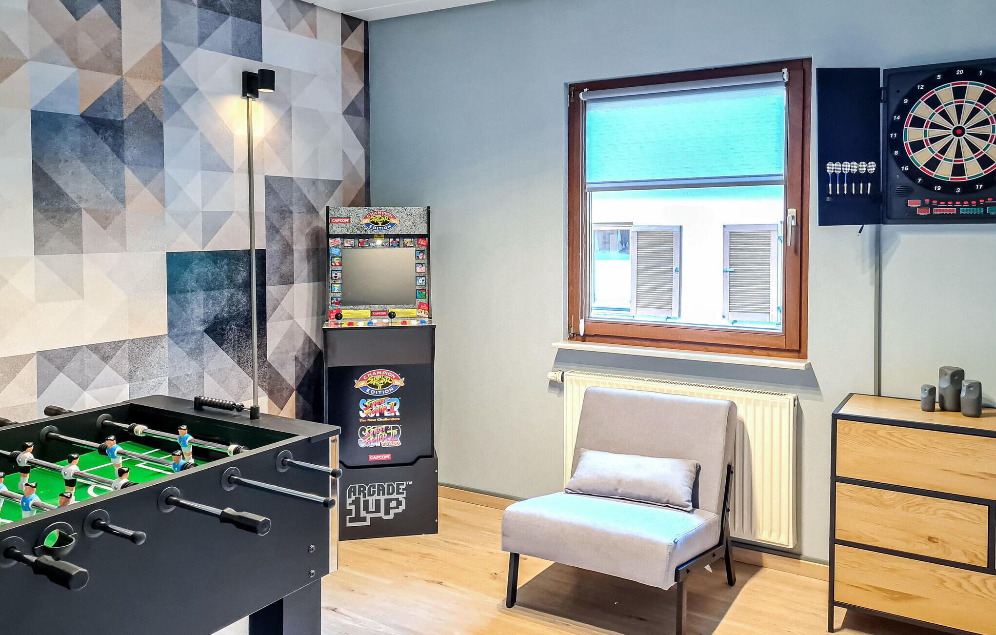 Une pièce avec une table de baby-foot, un jeu de fléchettes, une fenêtre avec des volets et un radiateur.