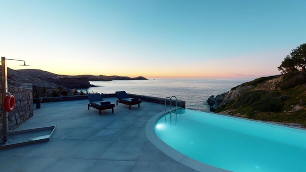 Zona de piscina con sillas de descanso y vista al mar al atardecer.