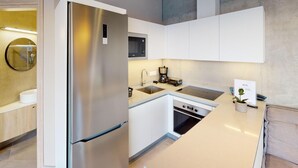 Una cocina moderna con armarios blancos, un refrigerador de acero inoxidable, un horno empotrado y una cafetera.