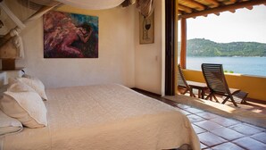 A bedroom with a bed, a painting, and a view of the sea. - The Estate at Pacific Vacation | StayPV Luxury Oceanfront with Staff (Zihuatanejo)