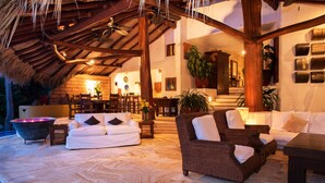 A cozy outdoor seating area with a thatched roof, wicker furniture, and a stone floor. - The Estate at Pacific Vacation | StayPV Luxury Oceanfront with Staff (Zihuatanejo)