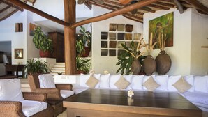 A spacious living area with a large wooden coffee table, wicker furniture, and multiple potted plants. - The Estate at Pacific Vacation | StayPV Luxury Oceanfront with Staff (Zihuatanejo)