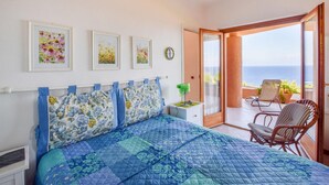 Une chambre à coucher comprenant un lit, une chaise, une table avec une lampe et un balcon avec vue sur la mer.