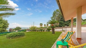 Eine Terrasse mit Blick auf das Meer, einer grünen Rasenfläche und Gartenmöbeln mit gelb-grün gestreiften Stühlen.