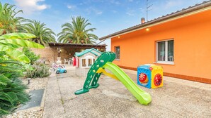 Ein Kinderspielbereich mit Rutsche und einem kleinen Spielhäuschen, umgeben von Palmen und einer Backsteinmauer.