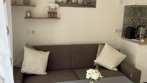 Un salon moderne avec un canapé marron, une table grise et un petit vase avec des fleurs. On y trouve des étagères ornées d’objets décoratifs et un tableau accroché au mur.