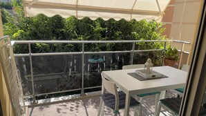 Un balcon avec une table et des chaises, une plante en pot et une grande fenêtre.