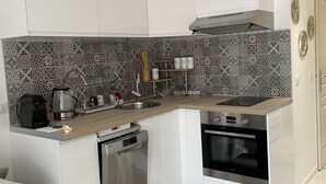 Une cuisine compacte avec des meubles blancs, un four encastré et une machine à café.
